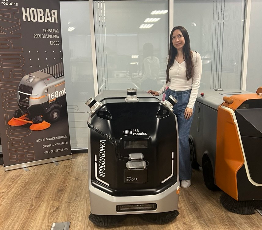 Mais Jamal standing beside the autonomous cleaning robot in an indoor display area.